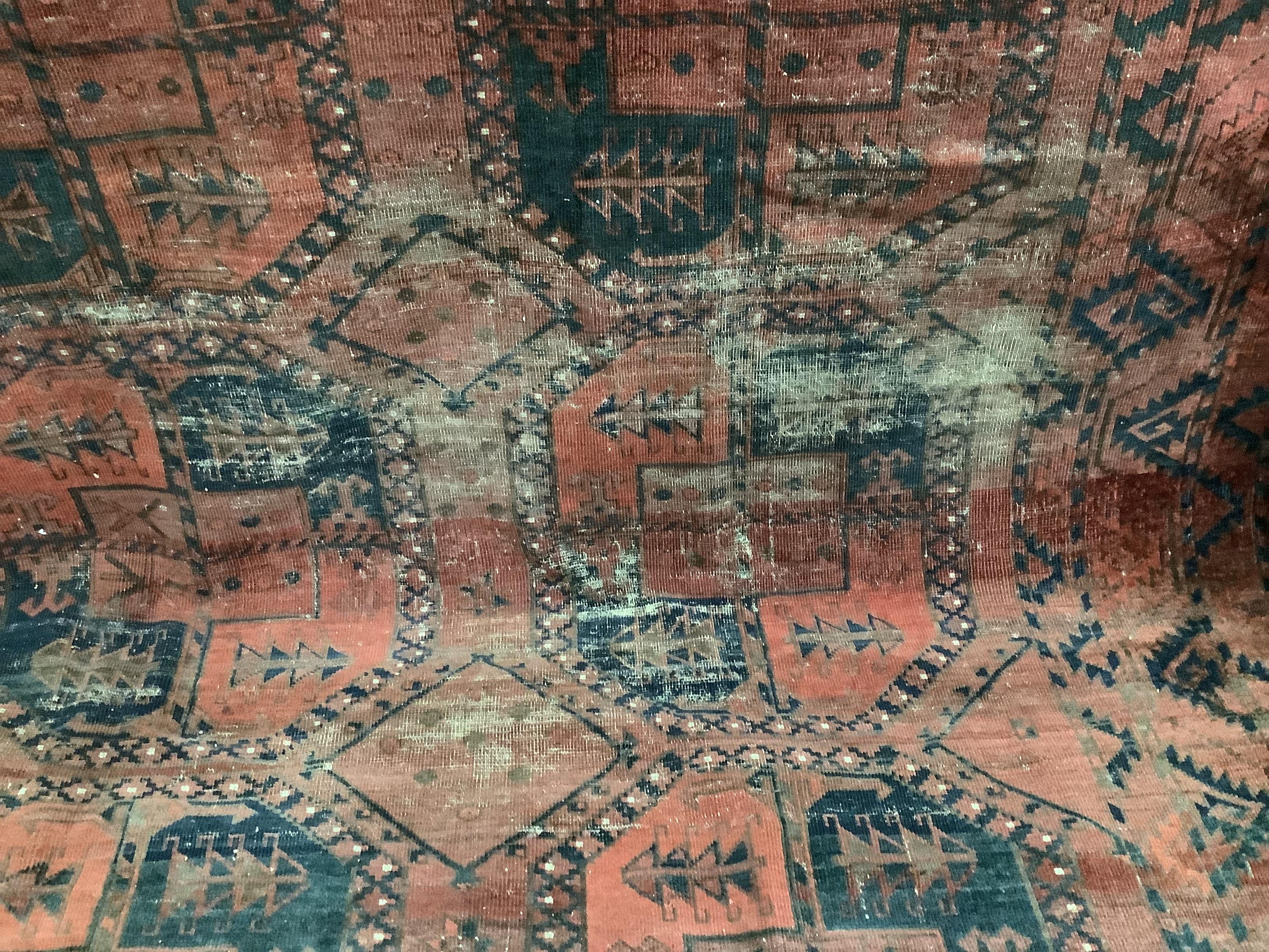 An antique Afghan red ground carpet, 340 x 278cm, worn and holed